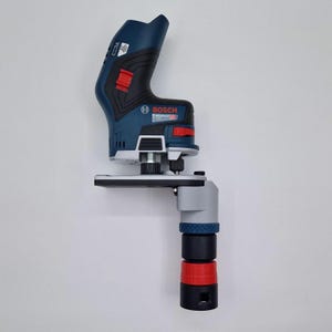 Könnte beinhalten: Ein blau-schwarzes Bosch Professional Elektrowerkzeug mit silberner Basis und einem vertikalen Aufsatz, der ein graues, blaues und rotes zylindrisches Bauteil aufweist. Das Gehäuse zeigt das Bosch-Logo und rote Schalter an der Seite.