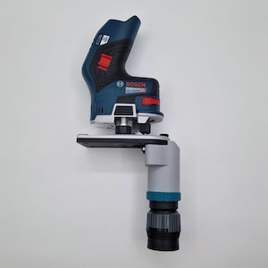Könnte beinhalten: Eine blau-schwarze Bosch Professional Kantenfräse mit rotem Schalter und silberner Metallbasis. An der Basis ist ein grauer, zylindrischer Staubabsaugstutzen mit einem strukturierten türkisfarbenen Ring und einem schwarzen Gewindeanschluss befestigt.
