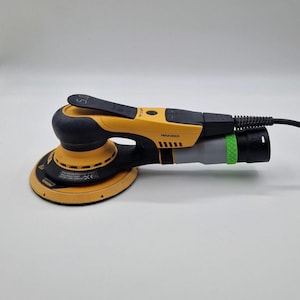 Könnte beinhalten: Ein gelb-schwarzer Elektroschleifer mit rundem Schleifpad. Der Schleifer hat einen schwarzen Griff und ein graues und schwarzes Netzkabel. Der Markenname "Mirka" ist auf der Seite sichtbar.