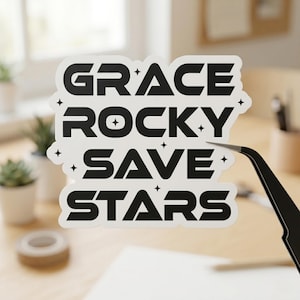 May include: A white sticker with the words "GRACE ROCKY SAVE STARS" in bold black letters. The sticker has a black border and small star graphics. A pair of black tweezers is holding the sticker.
