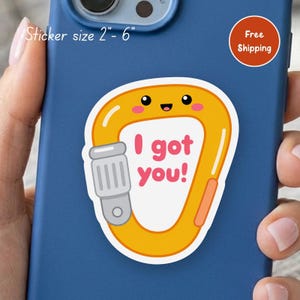 May include: A die-cut sticker featuring a yellow cartoon carabiner with a smiling face and pink cheeks. The center of the carabiner contains the pink text "I got you!" and a gray locking mechanism. The sticker size is listed as 2"- 6".