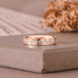 Op de afbeelding: Roségouden ring met een bloemmotief. De ring heeft een band met ingewikkelde blad- en bloempatronen, geaccentueerd met kleine, sprankelende edelstenen. De ring wordt gepresenteerd op een neutrale ondergrond, die de fijne details benadrukt.