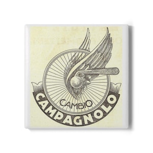 May include: A square tile featuring a vintage-style graphic illustration of a bicycle wheel with a large wing extending from the center. The text "CAMBIO" and "CAMPAGNOLO" is printed in a dark, bold font along a curved banner at the bottom.