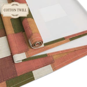 K&ouml;nnte beinhalten: Ein Baumwoll-Twill-Stoff mit einem Patchwork-Design aus rechteckigen Bl&ouml;cken in Olivgr&uuml;n, Terrakotta-Orange und Off-White. Das Textil ist teilweise aufgerollt und zeigt eine wei&szlig;e Unterseite sowie sichtbare N&auml;hte entlang der Kanten.