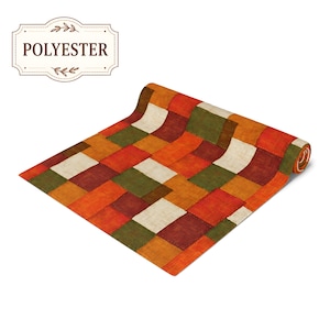 K&ouml;nnte beinhalten: Ein rechteckiger Tischl&auml;ufer mit einem Patchwork-Design aus abwechselnden Quadraten in den Farben Orange, Rot, Olivgr&uuml;n und Creme. Der Stoff weist eine sichtbare Webstruktur auf. Ein Etikett in der oberen linken Ecke zeigt den Text POLYESTER.