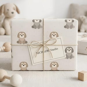 May include: A rectangular gift box wrapped in light beige paper featuring a repeating pattern of small gray and tan cartoon dogs. The package is tied with thin brown twine and includes a white rectangular gift tag labeled MICHA EBO Studio.
