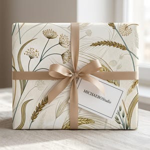 May include: A rectangular gift box wrapped in cream-colored paper featuring a botanical pattern of golden wheat stalks and delicate wildflowers. The package is tied with a smooth beige ribbon and includes a white tag printed with MICHAEBOStudio.