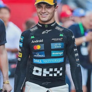 May include: A person wearing a yellow and navy blue cap and a black long-sleeve shirt with sponsor logos, including "Android", "Cisco", and "Dell Technologies". The shirt has a white and orange design at the waist.