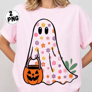 May include: A light pink t-shirt featuring a graphic of a ghost covered in a colorful floral pattern of orange, purple, and pink flowers. The ghost is holding an orange jack-o'-lantern candy bucket. A small circular badge says 2 PNG.
