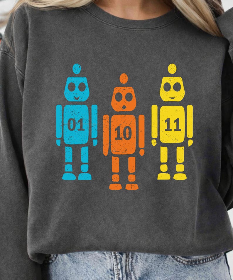 K&ouml;nnte beinhalten: Dunkelgraues Sweatshirt mit drei bunten Roboter-Grafiken. Die Roboter sind blau, orange und gelb, mit den Zahlen 01, 10 und 11. Das Design hat einen Used-Look.