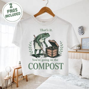 Op de afbeelding: Wit t-shirt met een grappige afbeelding van een kikker met een schort en een hooivork, met de tekst "That's it. You're going in the COMPOST." Het shirt bevat ook een "2 PNGs INCLUDED" afbeelding.