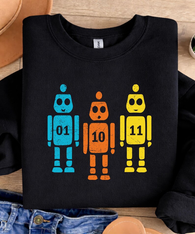 K&ouml;nnte beinhalten: Schwarzes Sweatshirt mit drei Roboter-Designs in Blau, Orange und Gelb. Jeder Roboter tr&auml;gt eine Nummer: 01, 10 und 11. Das Design ist einfach und auff&auml;llig, mit einem Retro-Look. Geeignet f&uuml;r Kinder und Roboter-Fans.
