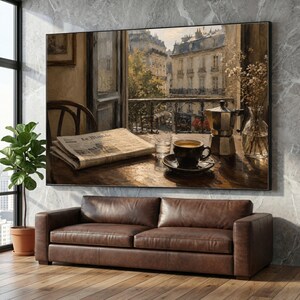 May include: A framed painting depicts a Parisian cafe scene. A table holds a cup of coffee, a newspaper, and a coffee maker. The view through the window shows buildings and a balcony. A brown leather sofa sits below the artwork.