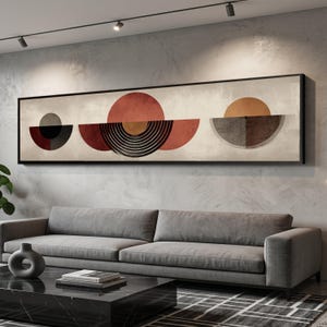 Könnte beinhalten: Abstrakte geometrische Wandkunst in einem schwarzen Rahmen. Das Kunstwerk zeigt eine Reihe von Halbkreisen und Kreisen in Rot-, Braun-, Grau- und Schwarztönen vor einem neutralen Hintergrund. Das Kunstwerk wird über einem grauen Sofa ausgestellt.