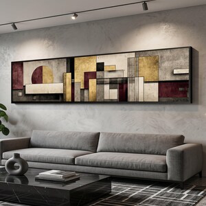 Puede incluir: Arte mural geométrico abstracto en un marco negro. La obra presenta una mezcla de formas y colores, incluyendo dorado, burdeos, gris y blanco. Cuelga sobre un sofá gris y una mesa de centro de mármol negro.