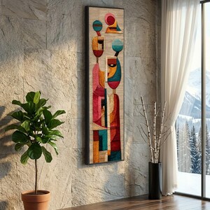 Könnte beinhalten: Abstrakte Wandkunst mit einem farbenfrohen geometrischen Design. Das Kunstwerk, in Schwarz gerahmt, zeigt Figuren mit roten, orangefarbenen, blauen und türkisfarbenen Akzenten. Es wird an einer strukturierten Steinmauer mit einer Topfpflanze und einem Fenster mit Blick auf einen schneebedeckten Berg ausgestellt.