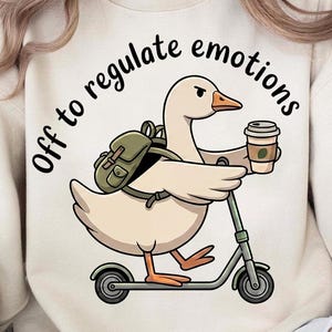 May include: Cream-colored sweatshirt featuring a cartoon goose riding a scooter and holding a coffee cup. The goose wears a backpack and the text "Off to regulate emotions" is arched above the goose. The design is printed on a soft, casual sweatshirt.