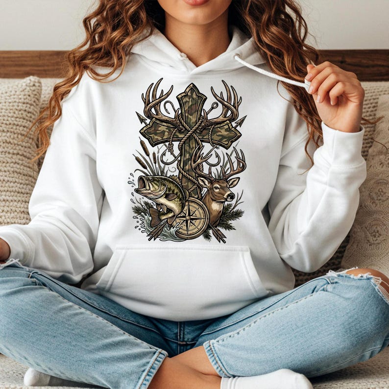 May include: White hoodie featuring a graphic design with a cross, deer antlers, a deer, a fish, and a compass. The cross has a camouflage pattern. The design incorporates fishing and hunting elements.