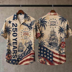 Puede incluir: Una camisa de manga corta con botones sobre un fondo beige con un estampado patriótico. El diseño incluye un retrato de George Washington, un velero, un águila, la bandera estadounidense, palmeras y el texto 250 YEARS 1776 2026.