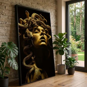 May include: A framed art print featuring a golden sculpture of Medusa with snakes for hair. The artwork is set against a black background, with the figure's face illuminated. The print is leaning against a brick wall, with plants in the foreground.