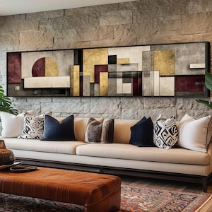 May include: Abstract geometric wall art in a black frame. The artwork features a mix of shapes and colors, including gold, burgundy, gray, and beige. The artwork is displayed above a beige sofa with decorative pillows.