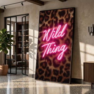 Peut inclure: Impression artistique encadrée avec un motif léopard et l'inscription "Wild Thing" en néon rose vif. L'œuvre est présentée dans un intérieur moderne aux couleurs neutres. Un élément décoratif.