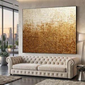 May include: Large framed artwork with a gold and white gradient design. The piece features raised, textured elements. It hangs above a beige, tufted sofa in a modern living room setting, creating a luxurious feel.