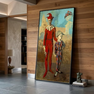 May include: A framed print of a painting featuring two figures in costume. One figure wears a red outfit with a tall hat, the other a harlequin suit. The background includes a blue sky and a decorative vase with flowers.