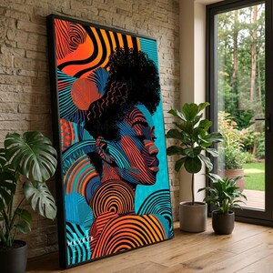 May include: A framed art print featuring a vibrant portrait of a person with black hair and a profile view. The artwork uses bold lines and colors, including orange, blue, and black. The print is leaning against a brick wall, with plants in the foreground.