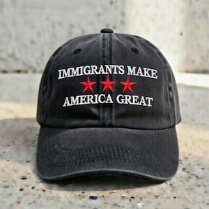 May include: A black baseball cap with the text "IMMIGRANTS MAKE AMERICA GREAT" in white lettering. Three red stars are positioned between the words "MAKE" and "AMERICA". The cap is made of a soft, worn material.