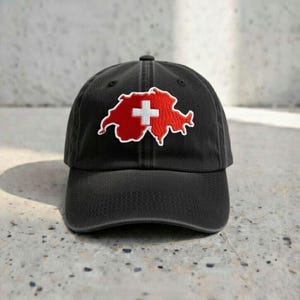 May include: Black baseball cap featuring an embroidered Swiss flag design. The flag is a red outline of the country with a white cross in the center. The cap has a curved brim and an adjustable strap.