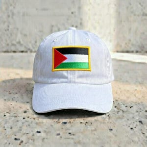 May include: White baseball cap featuring an embroidered patch of the Palestinian flag. The flag design includes a red triangle, black, white, and green stripes, and a yellow border. The cap is made of a soft fabric.