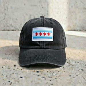 May include: A black baseball cap with a curved brim. The cap features a rectangular patch with the Chicago city flag, including four red stars and blue stripes. The cap is made of a soft, textured fabric.