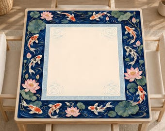 Op de afbeelding: Een vierkante tafelmat met een centraal crèmekleurig paneel omrand door een blauw kader met een geometrisch patroon. De rand toont een donkerblauw watermotief met oranje en witte koivissen, roze lotusbloemen en groene waterleliebladeren.
