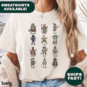 May include: Ivory-colored sweatshirt featuring a whimsical design of dogs dressed as fantasy characters, including a barbarian, wizard, and rogue. The text "SWEATSHIRTS AVAILABLE!" is at the top, and "SHIPS FAST!" is at the bottom.