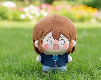 May include: A plush doll with brown hair, a navy blue top, and light blue shorts. The doll has a surprised expression with wide eyes and an open mouth. Two small gold hair clips are visible. The doll is standing on green grass.