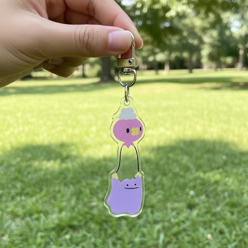 Pode incluir: Chaveiro de acr&iacute;lico transparente com um personagem de desenho animado. O personagem tem uma cabe&ccedil;a rosa, uma flor amarela e um corpo roxo. O chaveiro tem um fecho prateado e um pequeno anel para prender chaves. Um acess&oacute;rio divertido e colorido.