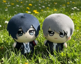 May include: Two plush dolls with large heads and round bodies. One doll has dark blue hair and a dark jacket with a white shirt, while the other has light gray hair and a similar dark jacket. Both feature embroidered eyes and small facial details.
