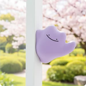 Op de afbeelding: Een lichtpaars, blob-vormig karakter met een lachend gezicht, leunend tegen een wit oppervlak. De achtergrond toont een vage tuin met groene struiken en roze bloesem bomen.