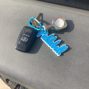 May include: A black Toyota RAV4 key fob and keys attached to a blue carabiner and a white and blue "Pickleball" keychain. The keychain has a pickleball paddle design.