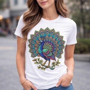 May include: White t-shirt featuring a colorful peacock design. The peacock is depicted with vibrant blue, green, purple, and yellow feathers, perched on a branch with green leaves. The shirt is a classic crew neck style.