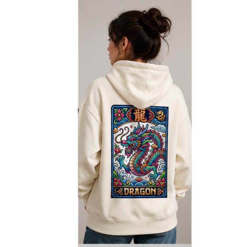 May include: Cream-colored hoodie with a colorful dragon graphic on the back. The dragon is depicted in shades of blue, green, and red, with the word "DRAGON" below. The hoodie has a drawstring hood and a kangaroo pocket.