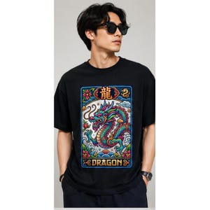 May include: Black t-shirt featuring a colorful dragon design with the word "DRAGON" at the bottom. The dragon is depicted in shades of blue, green, and red, with floral and wave-like elements. The shirt has short sleeves.