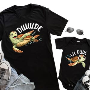 May include: Black t-shirts and a baby onesie with matching turtle graphics. The adult shirt says "DUUUUDE" and the baby onesie says "LIL DUDE". The turtle is green and brown.