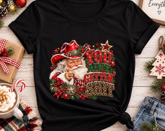 Puede incluir: Una camiseta negra de manga corta con un gráfico de Santa Claus con un sombrero de vaquero rojo con estampado de leopardo. Santa señala hacia adelante con el texto "YOU AIN'T GETTIN' SHIT" en letras rojas y de leopardo.