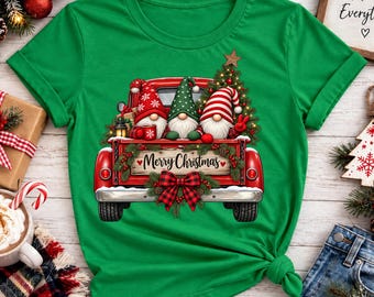 Puede incluir: Una camiseta verde brillante con un gráfico de una camioneta roja que transporta tres gnomos, un árbol de Navidad decorado y un letrero de madera que dice Merry Christmas con un lazo de cuadros rojos y negros en el portón trasero.