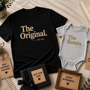 Może przedstawiać: Czarny t-shirt z napisem The Original. EST. 2026 w kolorze beżowym oraz szare body niemowlęce z napisem The Remix. EST. 2026 w kolorze beżowym. Zestaw zawiera czarne pudełko prezentowe z napisem BEST TEAM EVER. oraz dwie beżowe etykiety z tekstem.