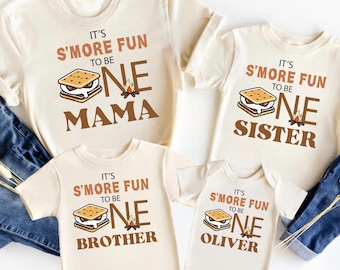 Puede incluir: Cuatro camisetas color crema y un body con un gráfico de s'mores y el texto "It's S'more Fun to be One". Las camisetas dicen "Mama", "Sister" y "Brother". El body dice "Oliver".