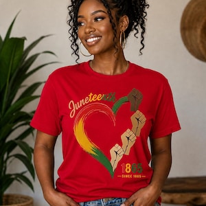 May include: Red t-shirt with a heart-shaped design in the colors of the Pan-African flag, featuring the word "Juneteenth" and the year "1865". The design includes raised fists. The shirt is worn by a person.