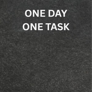 May include: A dark gray textured background with the white text "ONE DAY ONE TASK" in a sans-serif font. The text is centered and takes up a significant portion of the image.